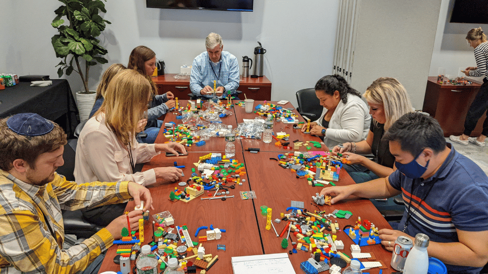 A focused group of professionals engaging in a LEGO Serious Play workshop, collaboratively building models to visualize concepts and solve challenges
