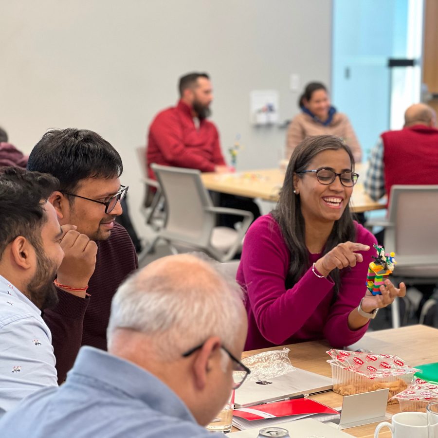 Engineer presenting her LEGO model to attentive teammates, showing how LEGO Serious Play transforms technical discussions into engaging experiences where team members actively listen and respond positively to shared ideas