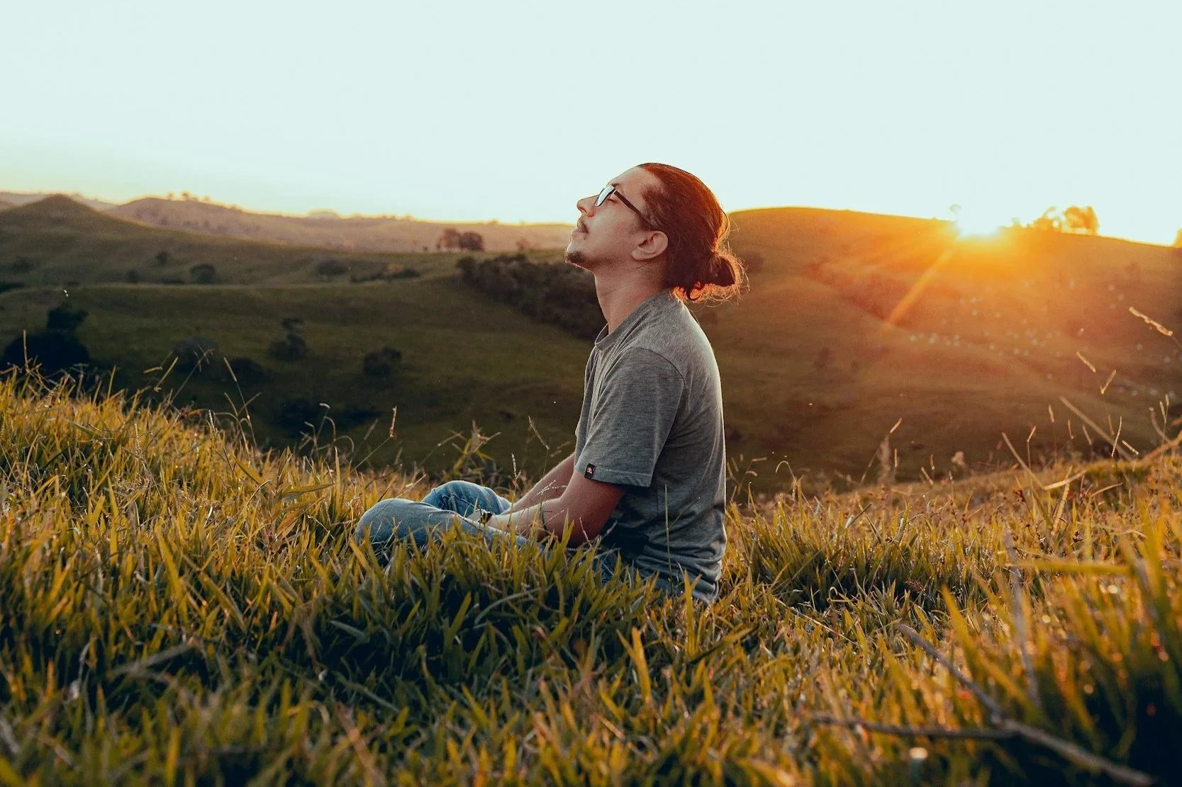 a person meditates in a field at sunset.