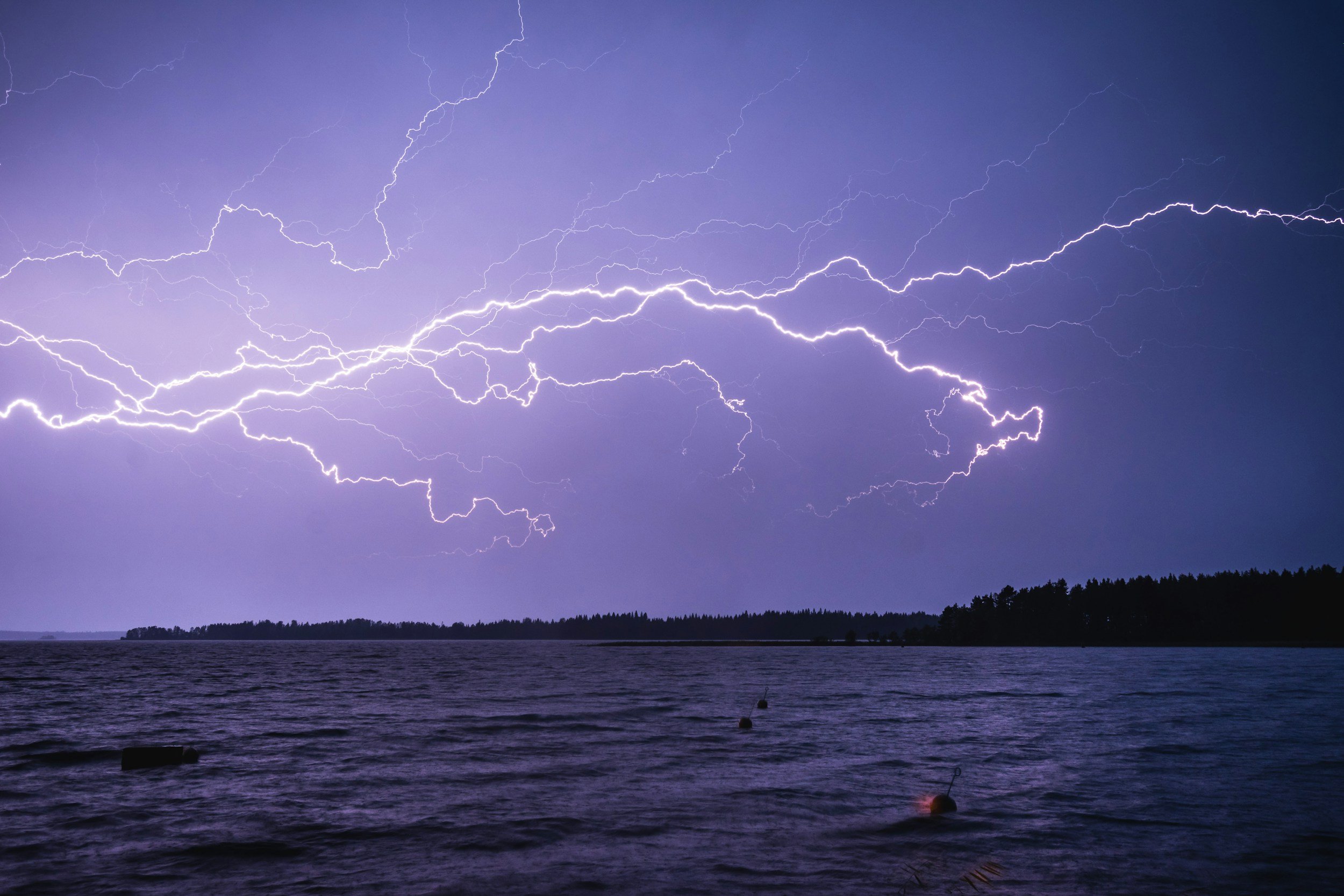 lighting spreads across a purple night sky over a body of water.