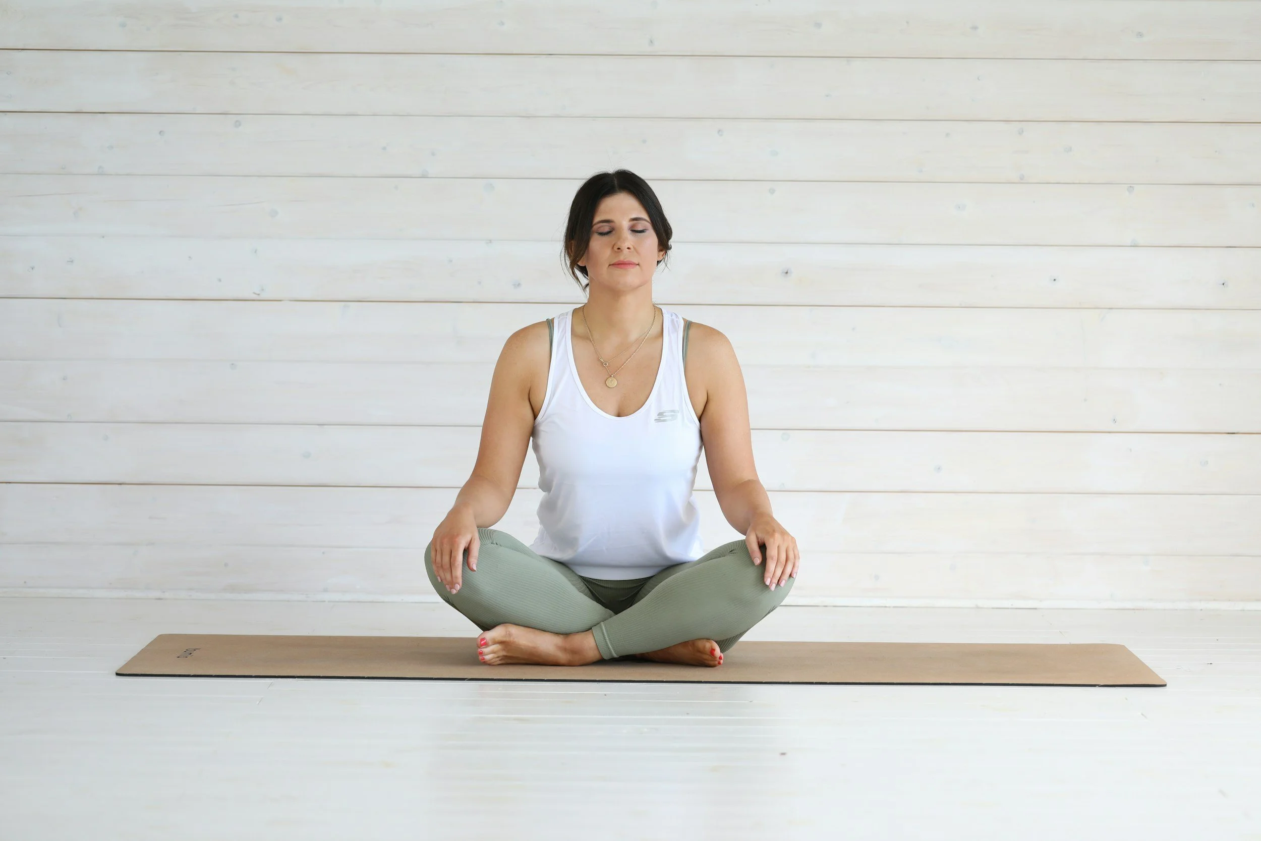 a person sits on a yoga mat in a brighly lit room with soft wooden walls.