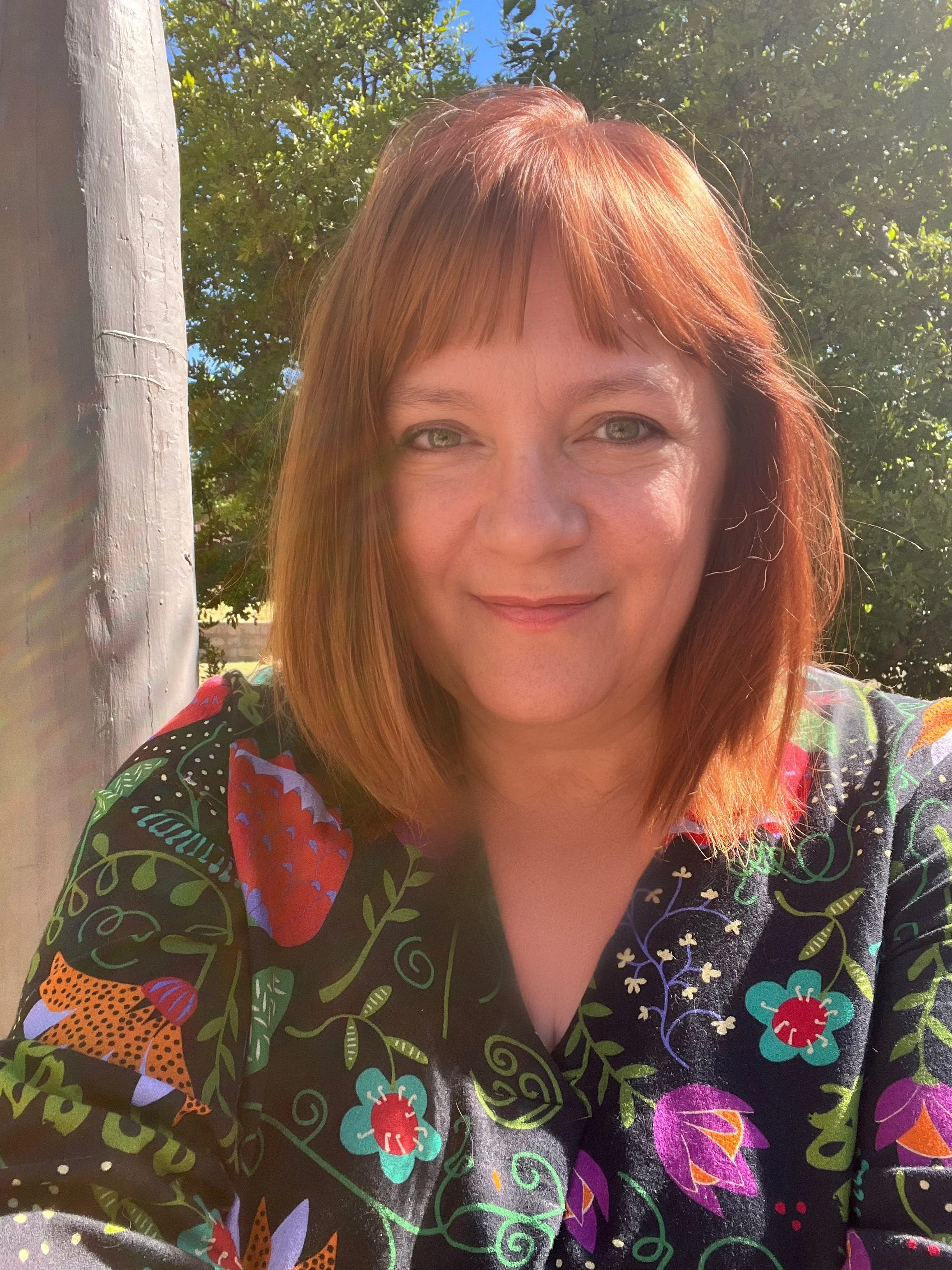 Valarie outdoors, with green foliage and a blue sky in the background.