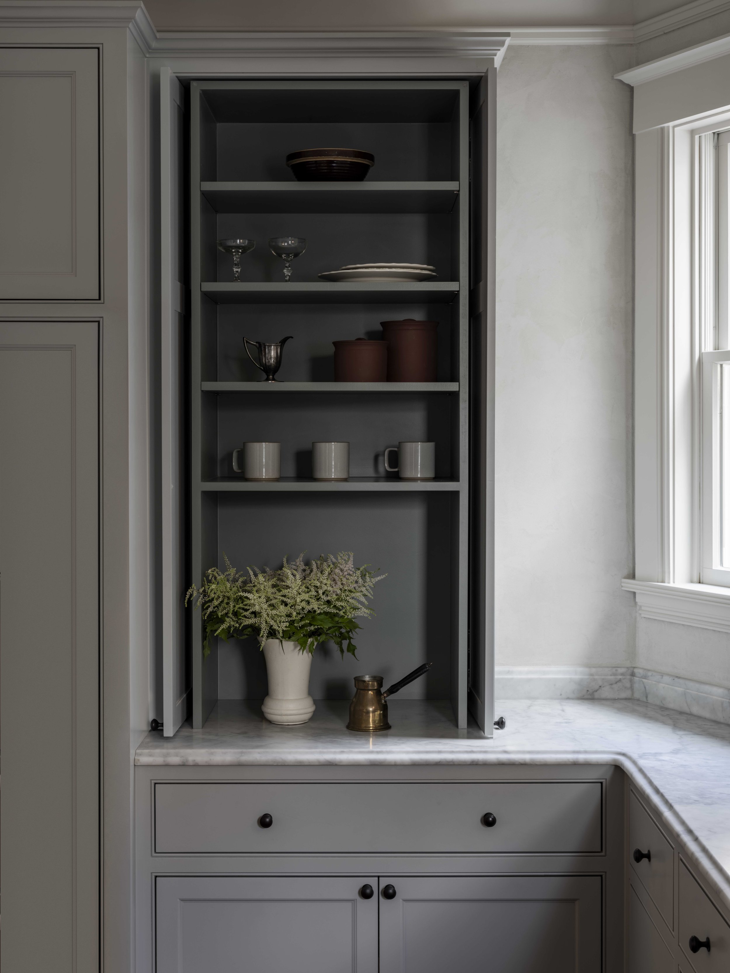 An open kitchen cabinet reveals cups, plates, and vase of flowers.