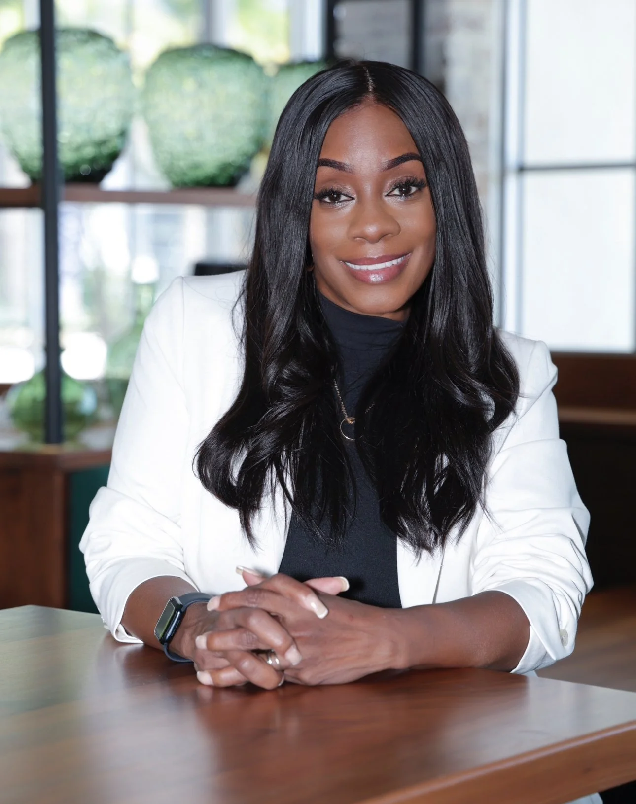Businesswoman sitting at a table with a smile, in a modern office setting.