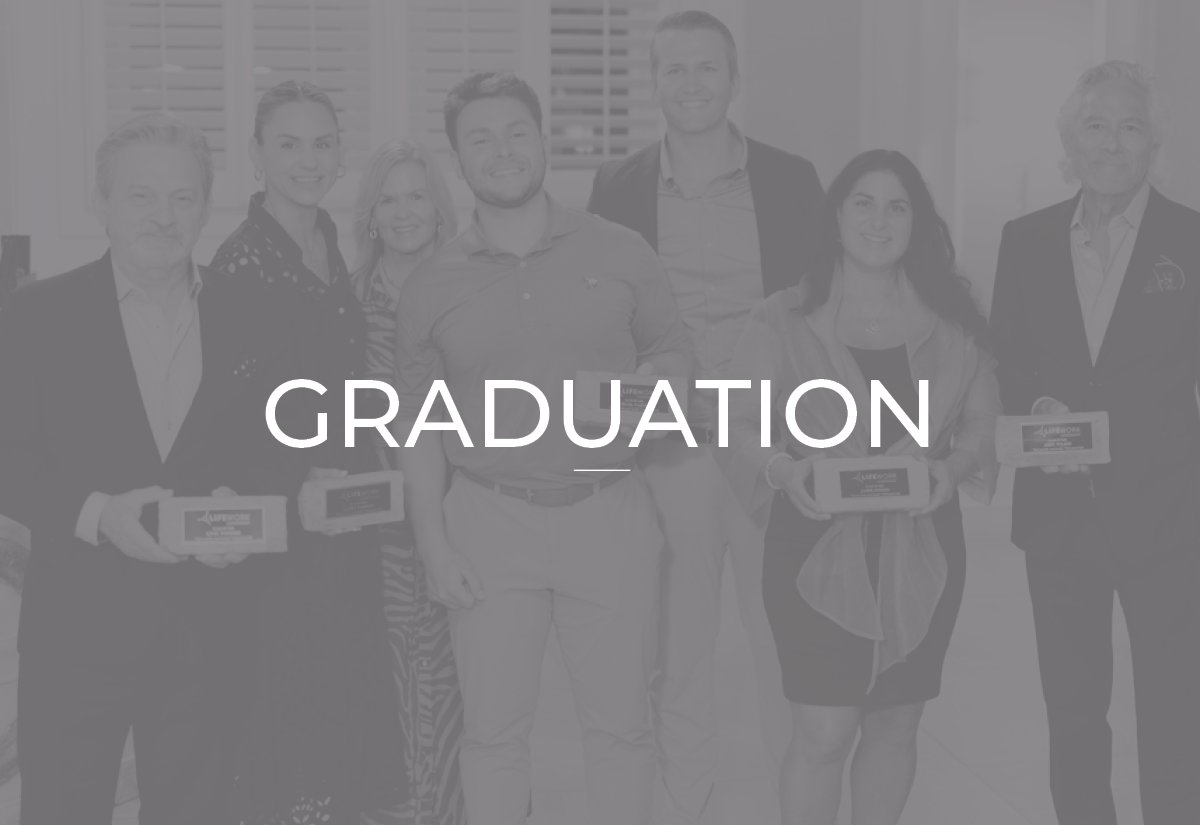 Group of people celebrating graduation, holding plaques, in a room with window blinds.