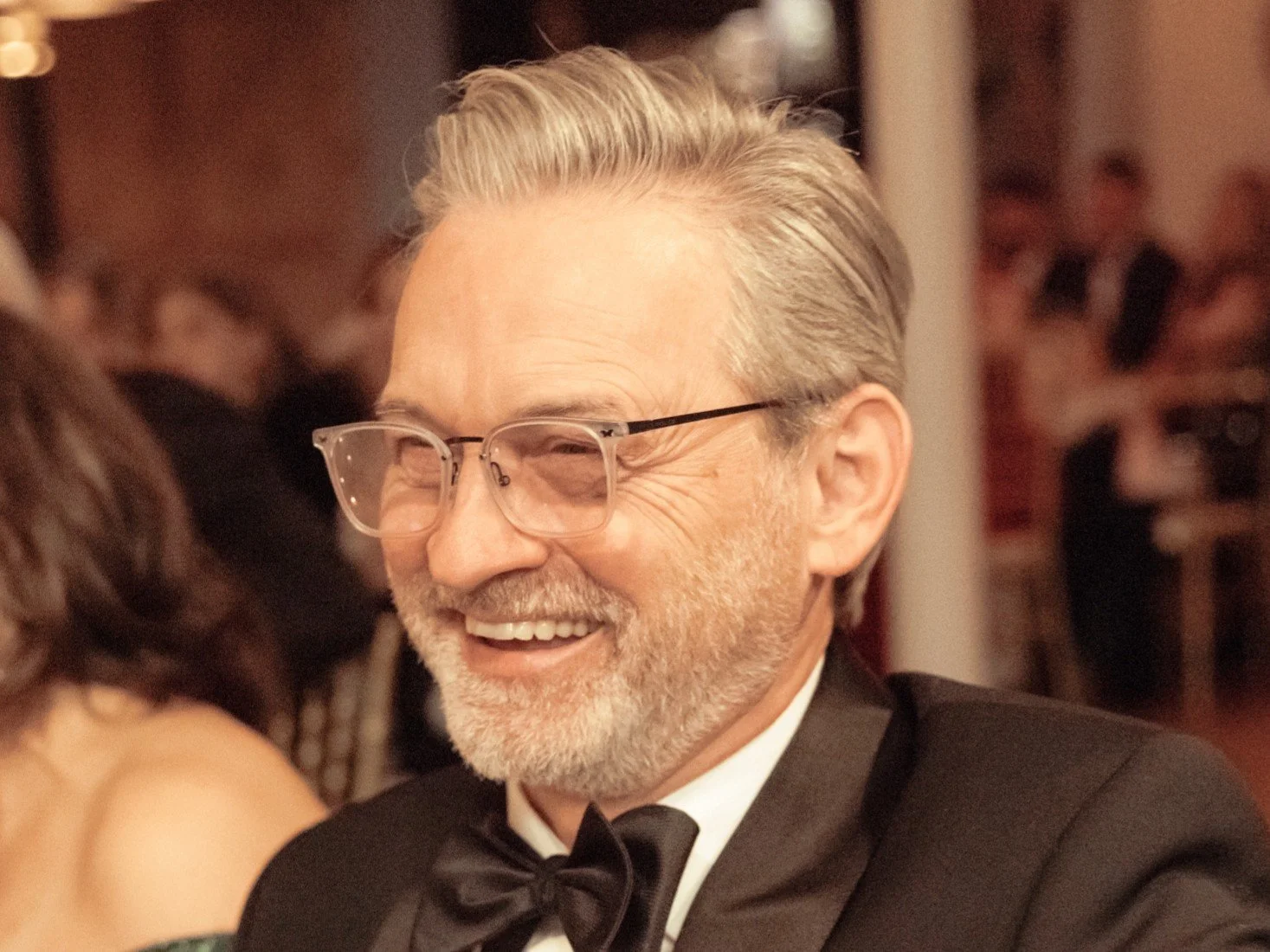 A middle-aged man with gray hair and glasses, smiling at a formal event, wearing a black tuxedo with a bow tie.