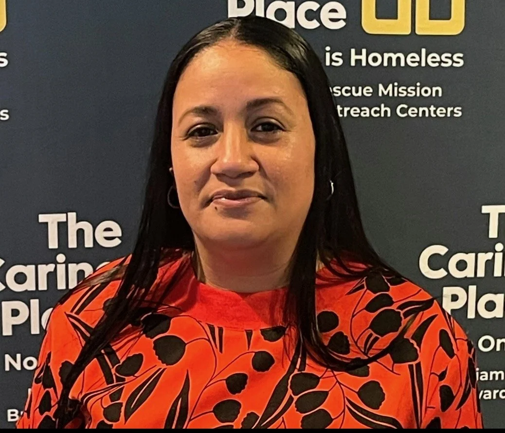 A woman with long dark hair wearing a red blouse with black leaf pattern, standing in front of a dark background with white text about homelessness and clinical care.