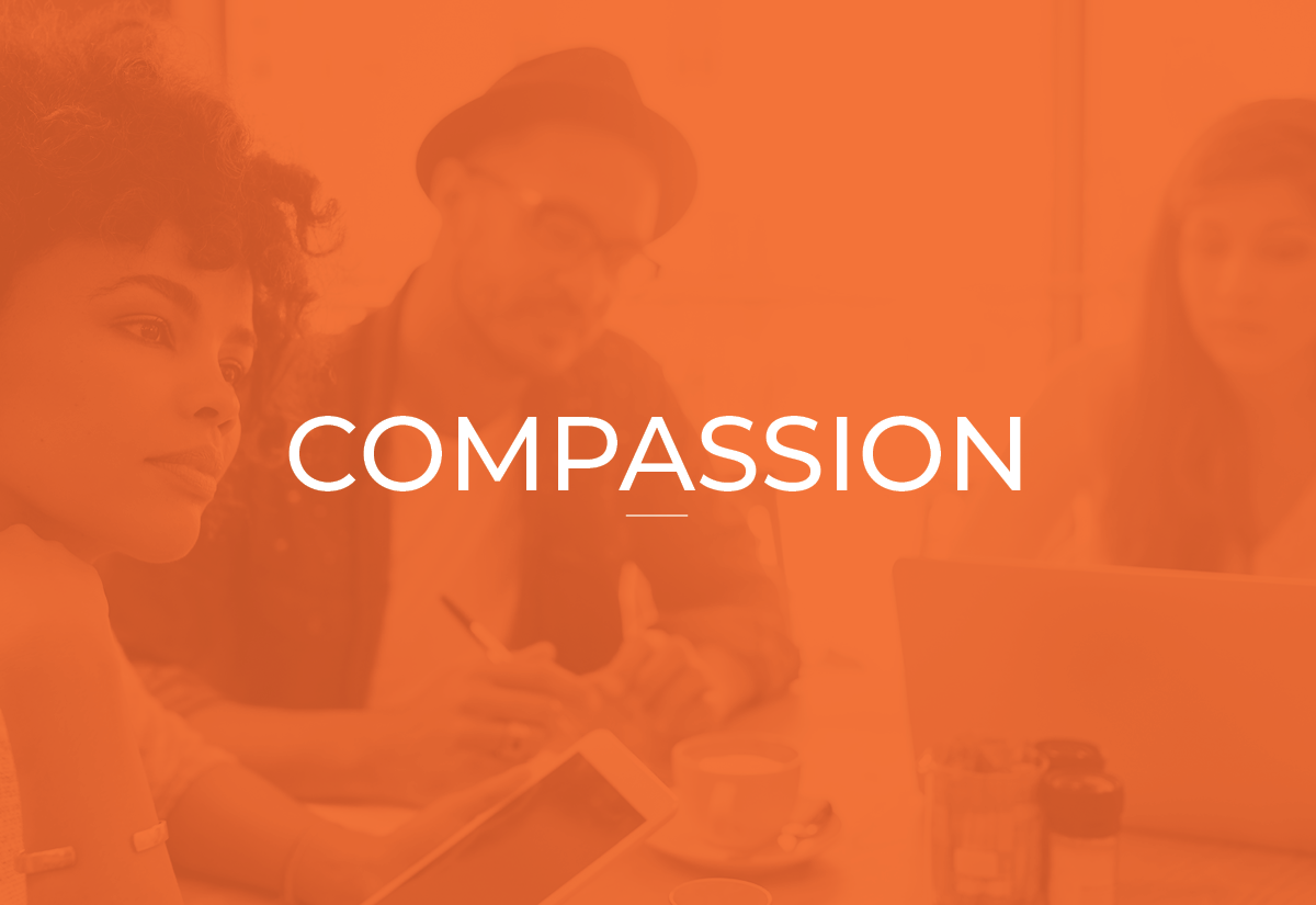 Three people sitting around a table in a meeting room, with the word 'COMPASSION' overlaid.