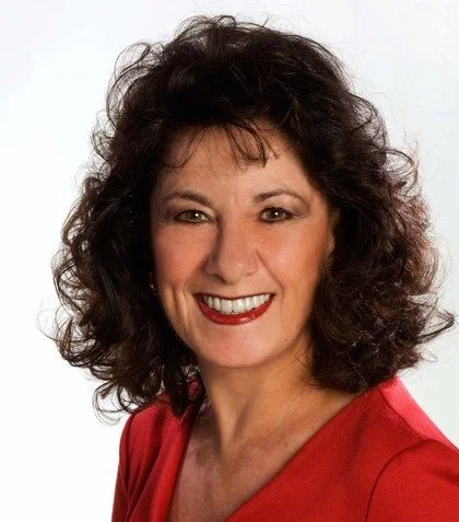 A woman with curly dark brown hair smiling, wearing a red top, against a plain white background.