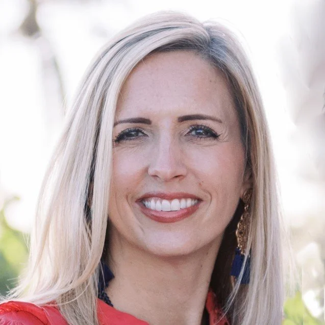 Close-up of a woman with blonde hair smiling outdoors.