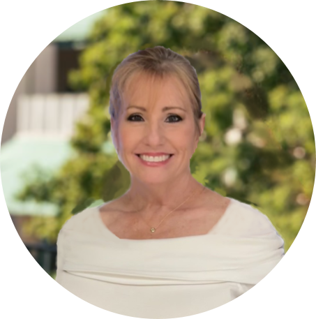 Smiling woman with blonde hair and a white top standing outdoors with green trees in the background.