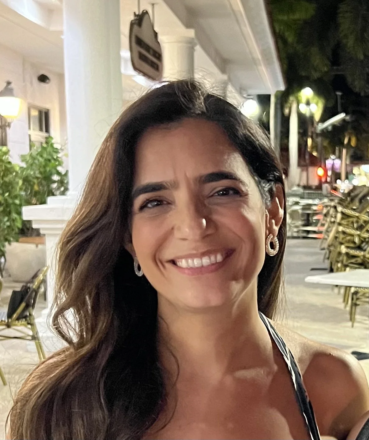 A woman smiling outdoors at night, with streetlights and trees in the background.