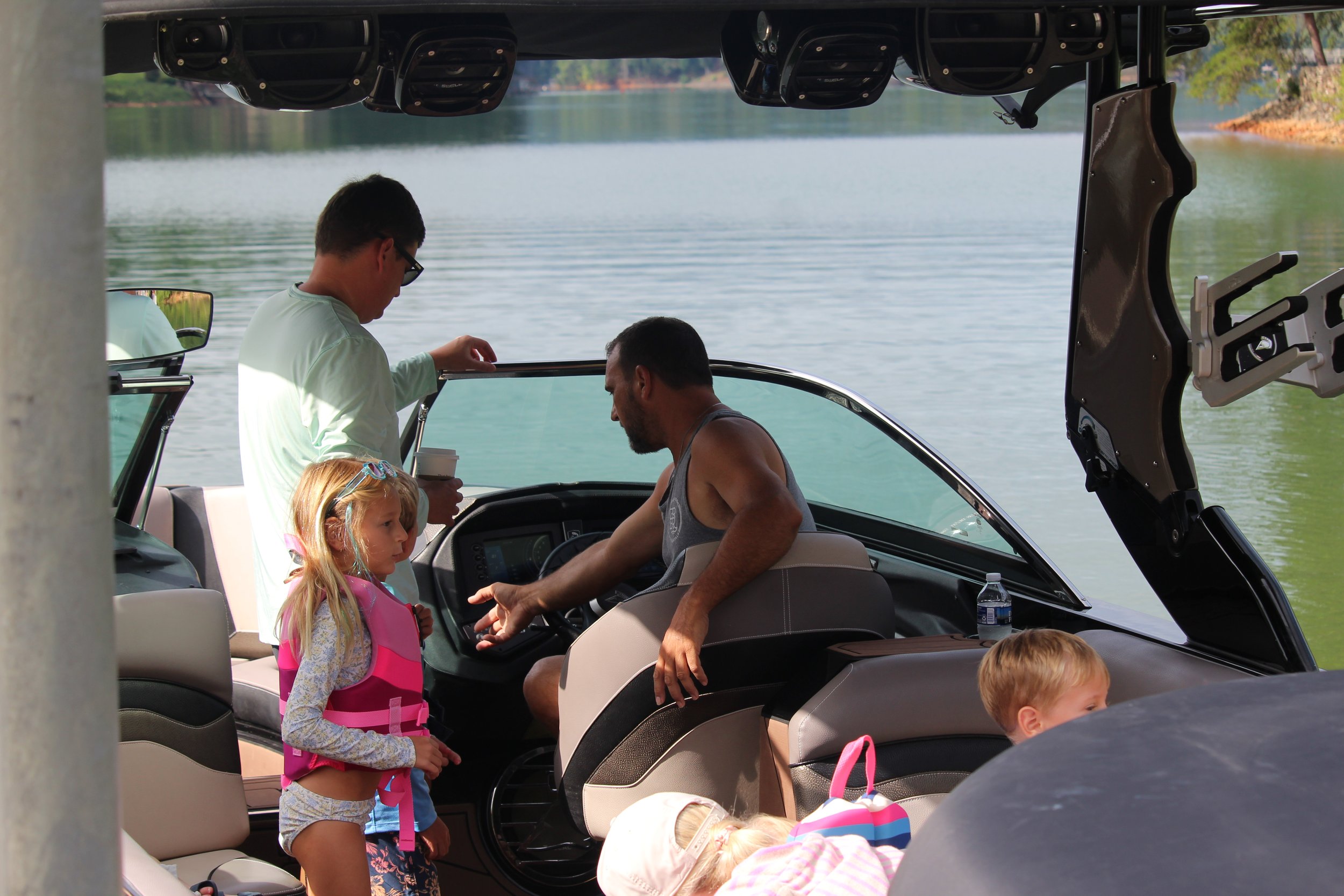 A group of people, including children and an adult, on a boat near a body of water, with trees in the background.