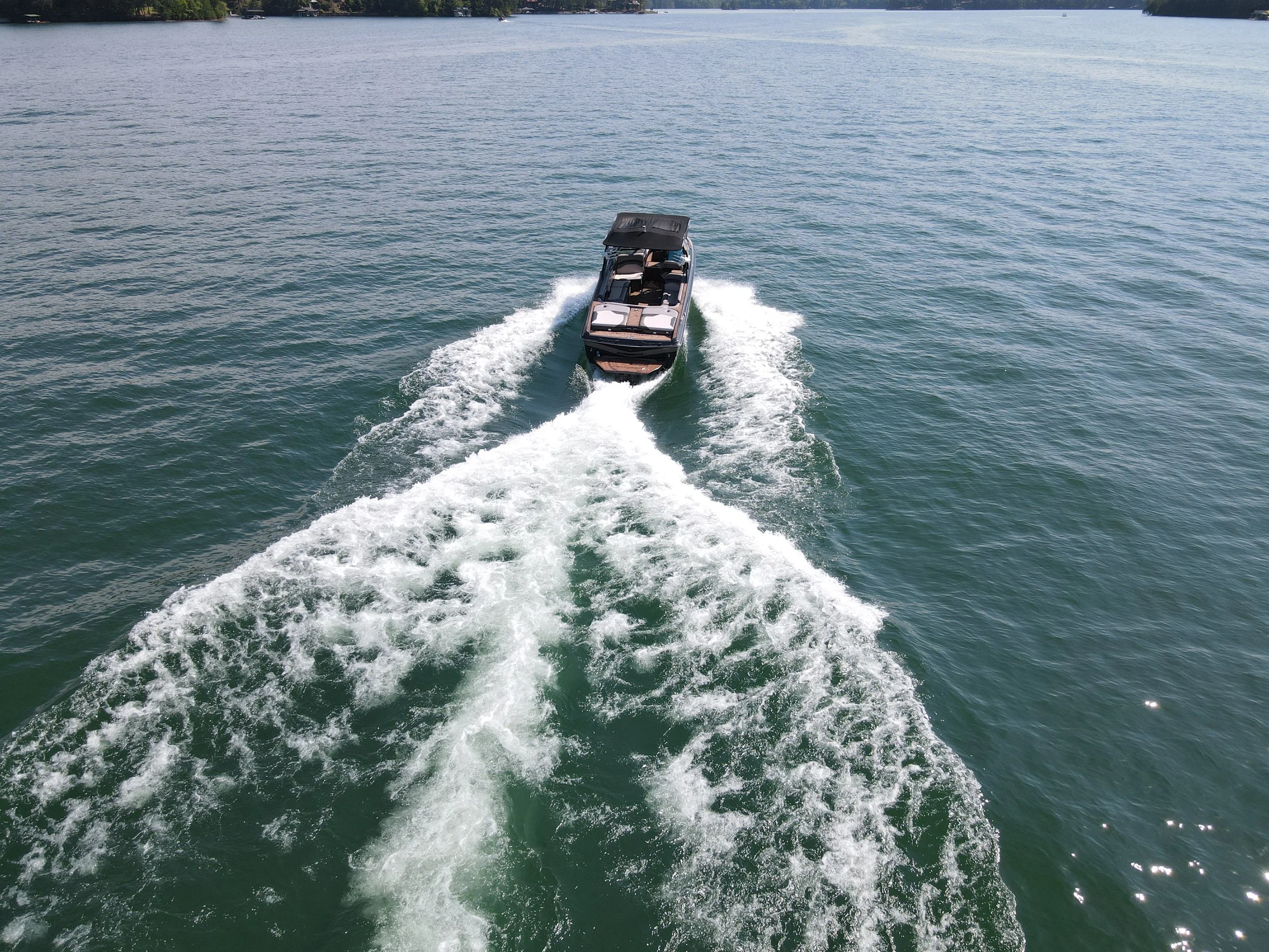 A boat moving across a large body of water, creating a wake behind it, with trees visible in the background.