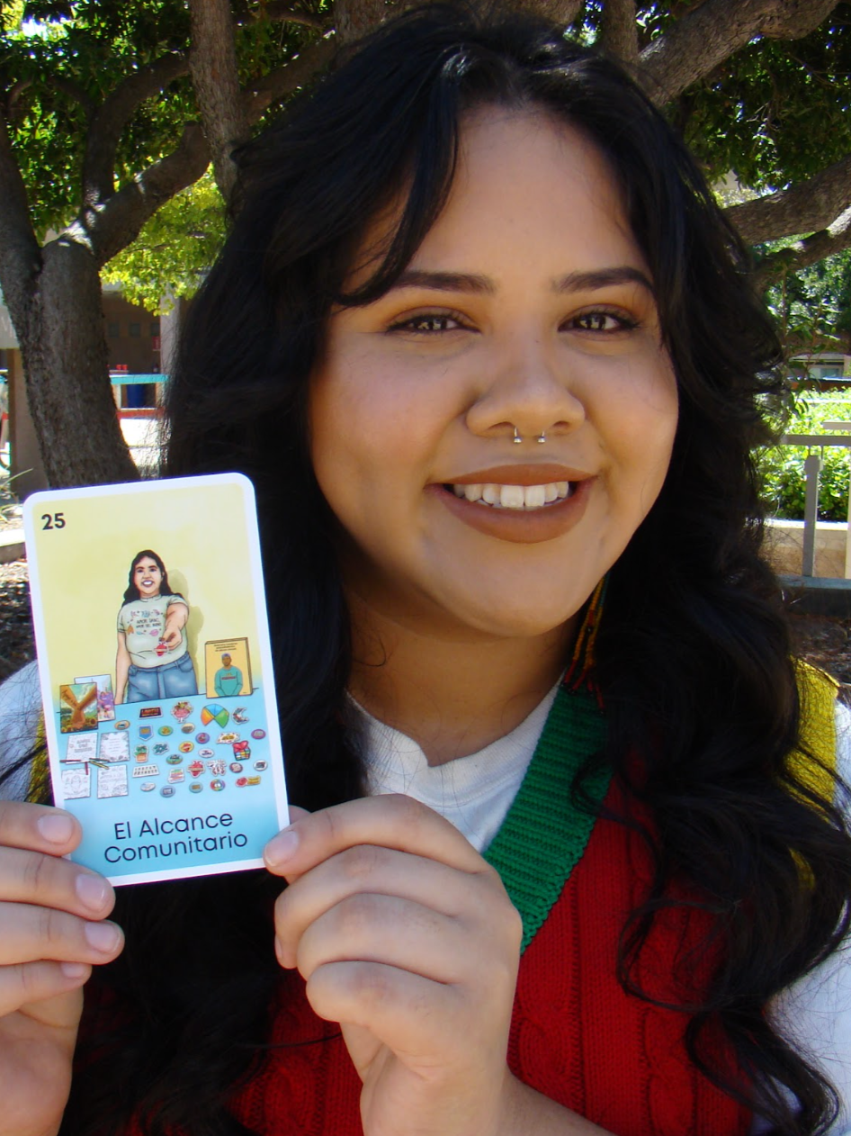 A smiling person with dark hair holding up a loteria card from RVCC's sexual violence prevention loteria game.
