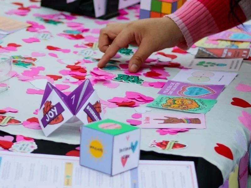 Person arranging pink and red paper hearts on table with Consent-Centered Valentine's Day cards and decorations.