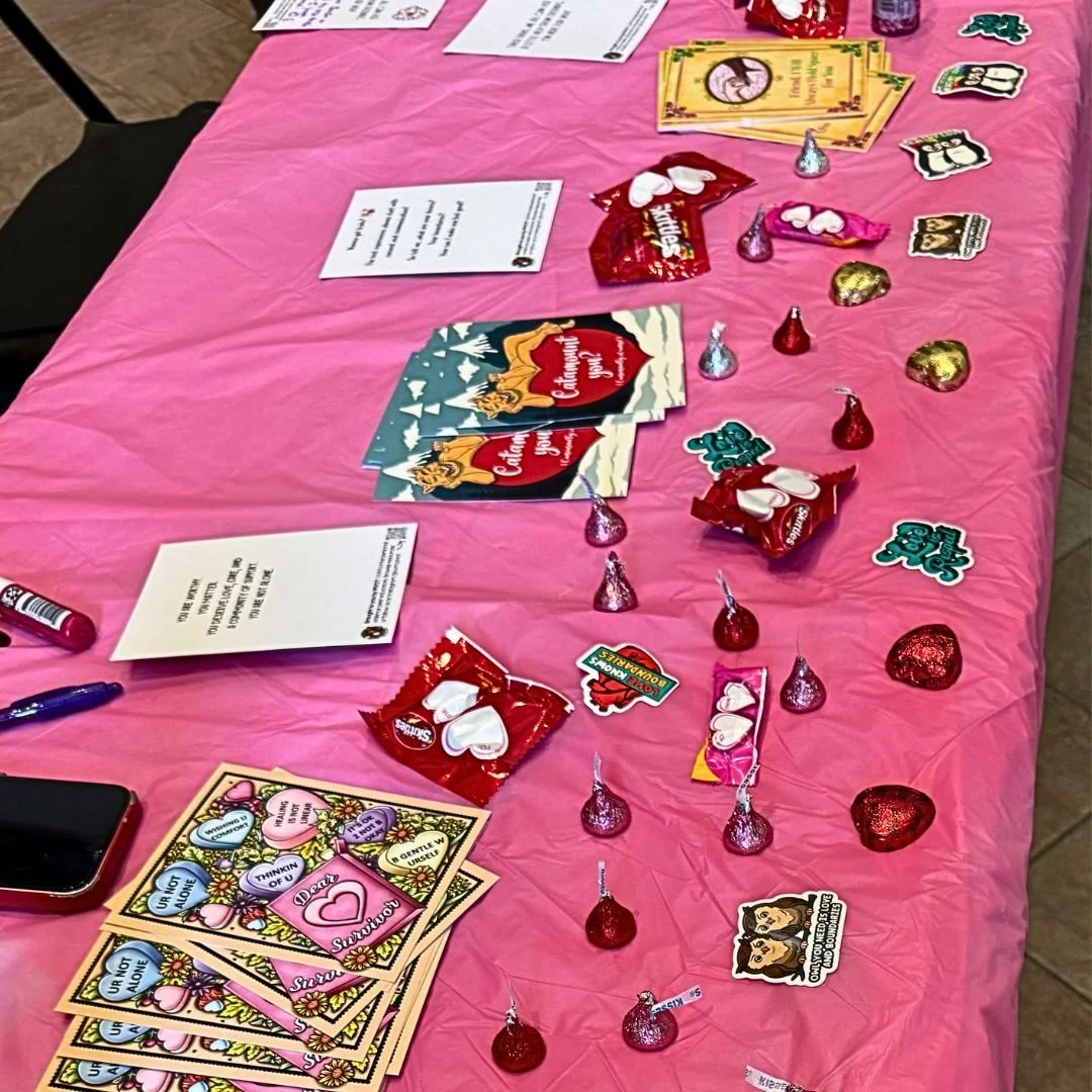 Table with pink tablecloth displaying Valentine's Day cards, assorted candies including Hershey's Kisses and Skittles, and decorative stickers.