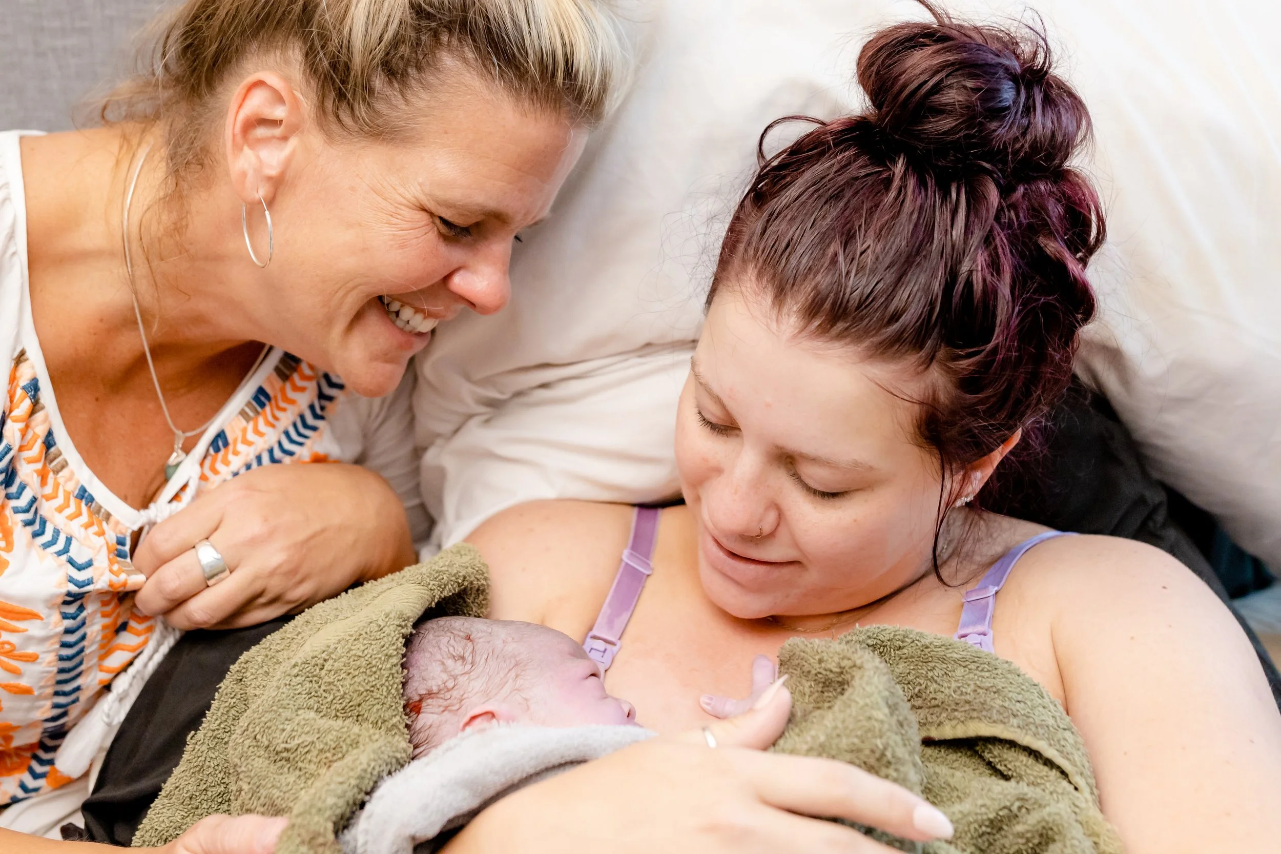 Young mother holding her newborn with her mother looking on smiling.