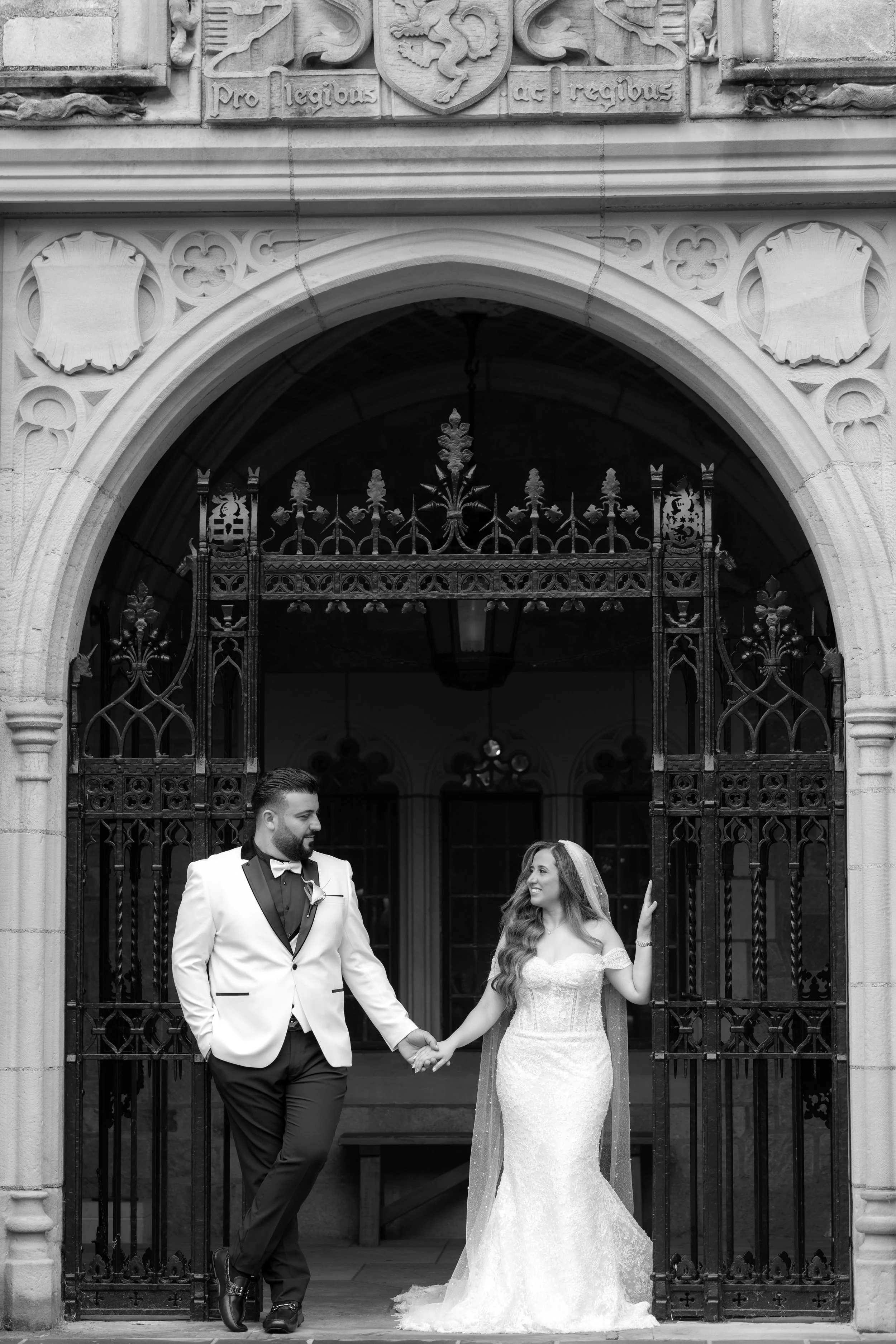 Black and white portrait of a couple holding hands beneath a carved stone archway