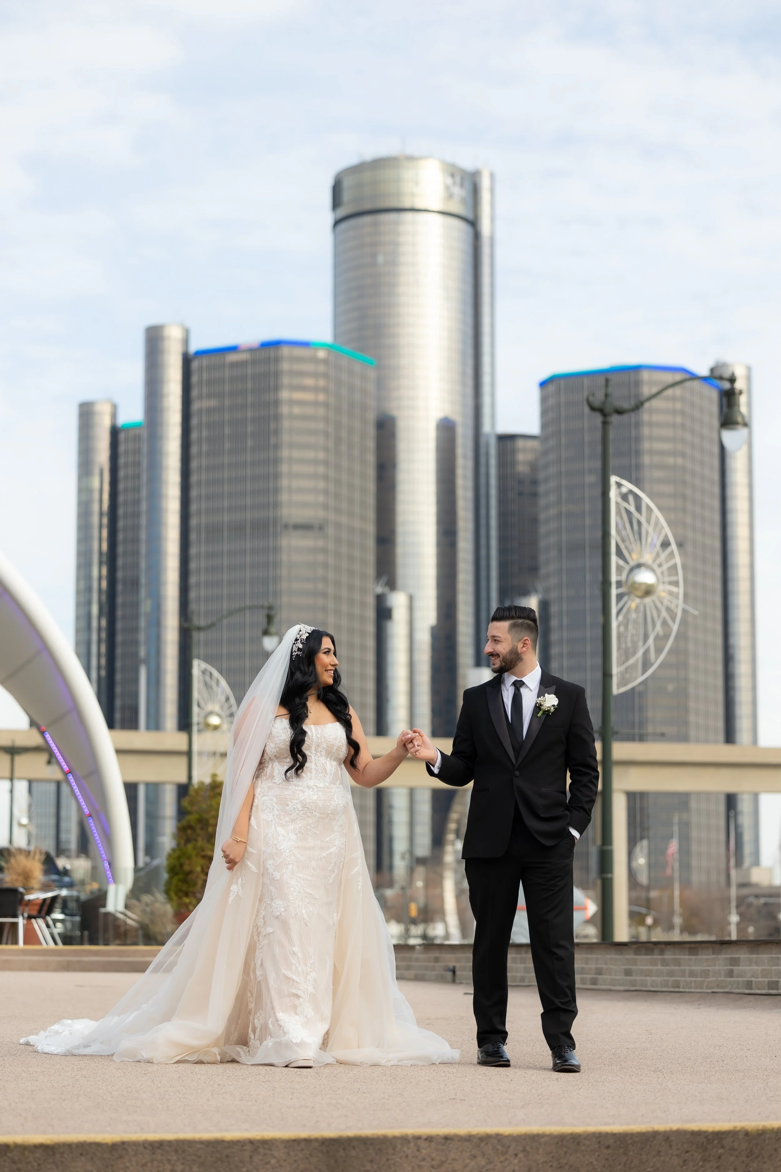 Bride and groom holding hands with the Detroit Renaissance Center skyline behind them