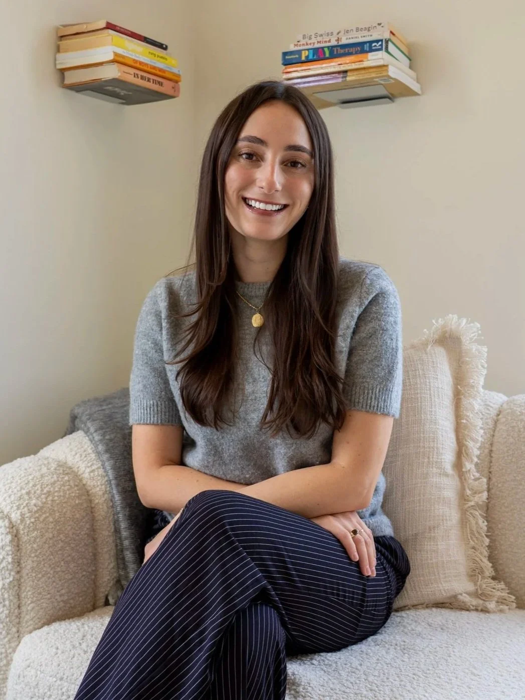 A woman with long brown hair sitting at a desk in an office, smiling at the camera.