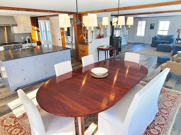 Open-concept dining and living area with a wooden dining table and white chairs, a kitchen with light blue cabinets, and a living room with a blue sofa and wooden flooring.