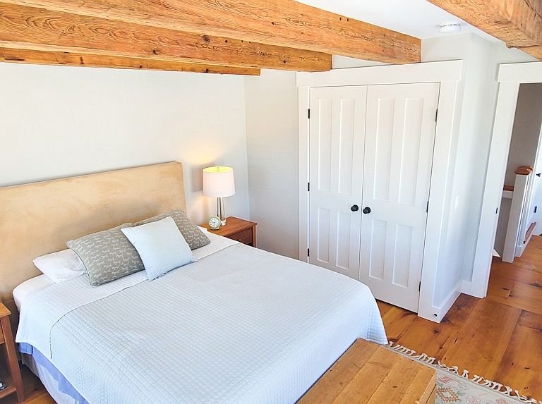 Bedroom with a bed, nightstand, and lamp, with a closet door and wooden ceiling beams.
