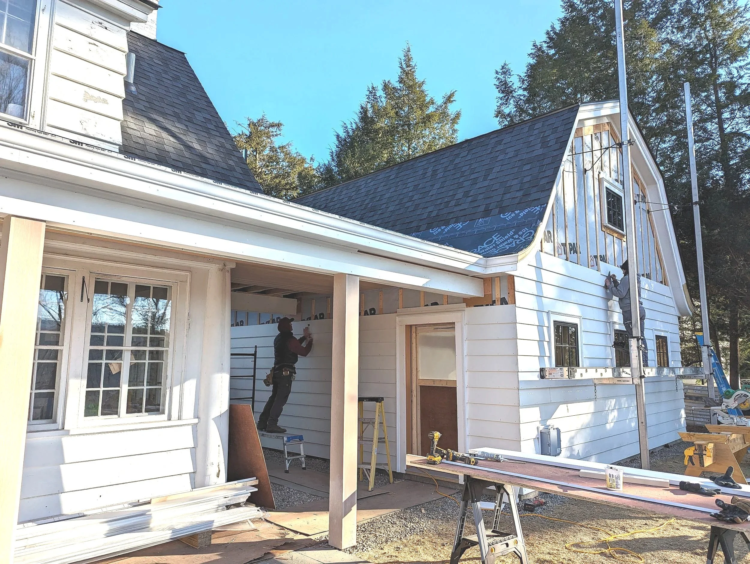Construction workers installing siding on a house with scaffolding and tools present.