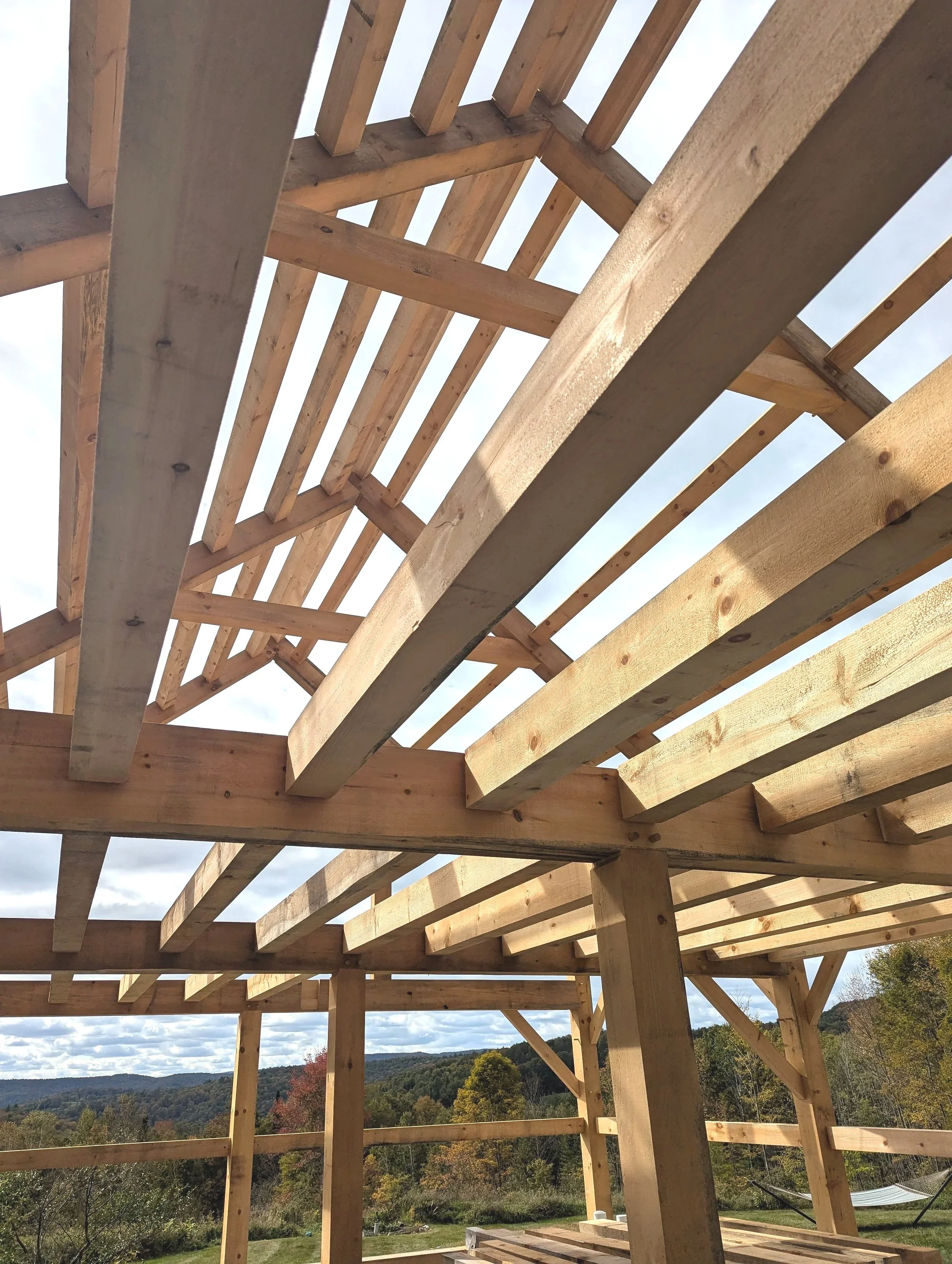 View of a wooden house frame under construction with a landscape of trees and hills in the background.