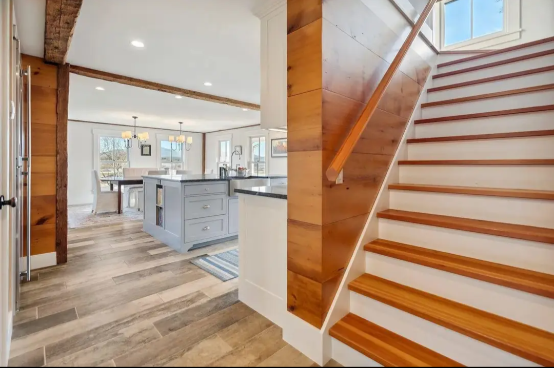 View of a modern kitchen and dining area with wooden flooring, a staircase with wooden steps and a window.