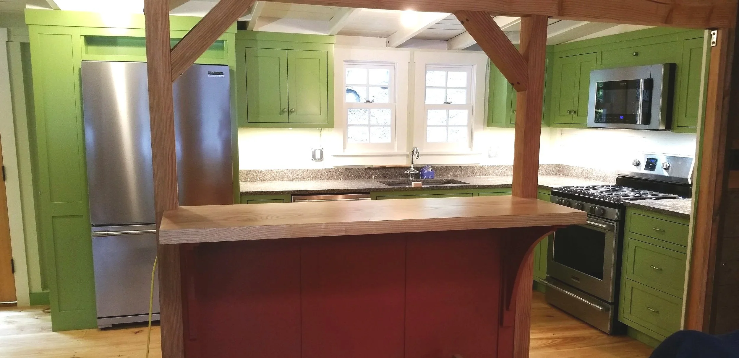 Kitchen with green cabinets, granite countertops, stainless steel refrigerator and stove, microwave, window above the sink, and a wooden breakfast bar