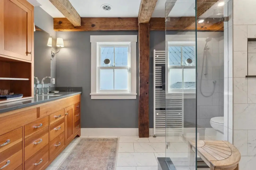 Bathroom with wooden cabinetry, gray walls, a window, and a glass-enclosed shower area.