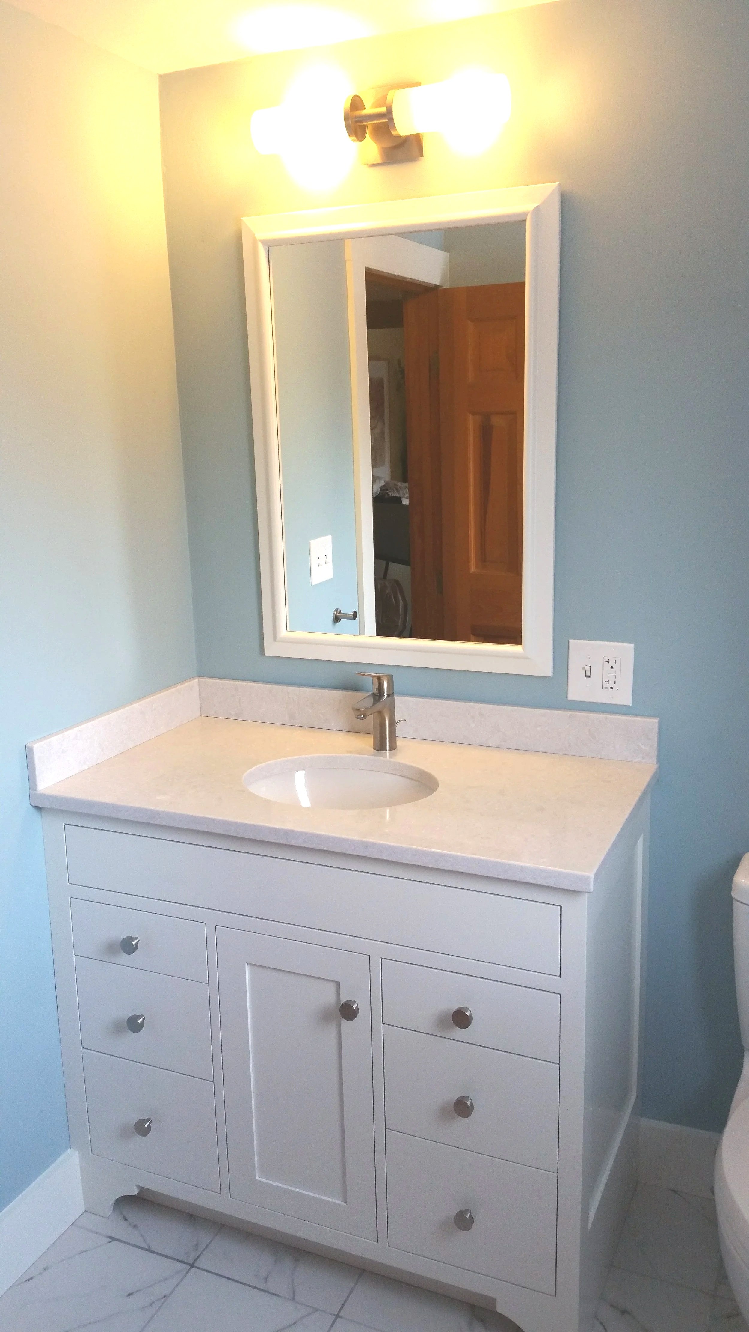 Bathroom vanity with a mirror above, a light fixture with two bulbs, a white cabinet with six drawers, a single sink, and a silver faucet.