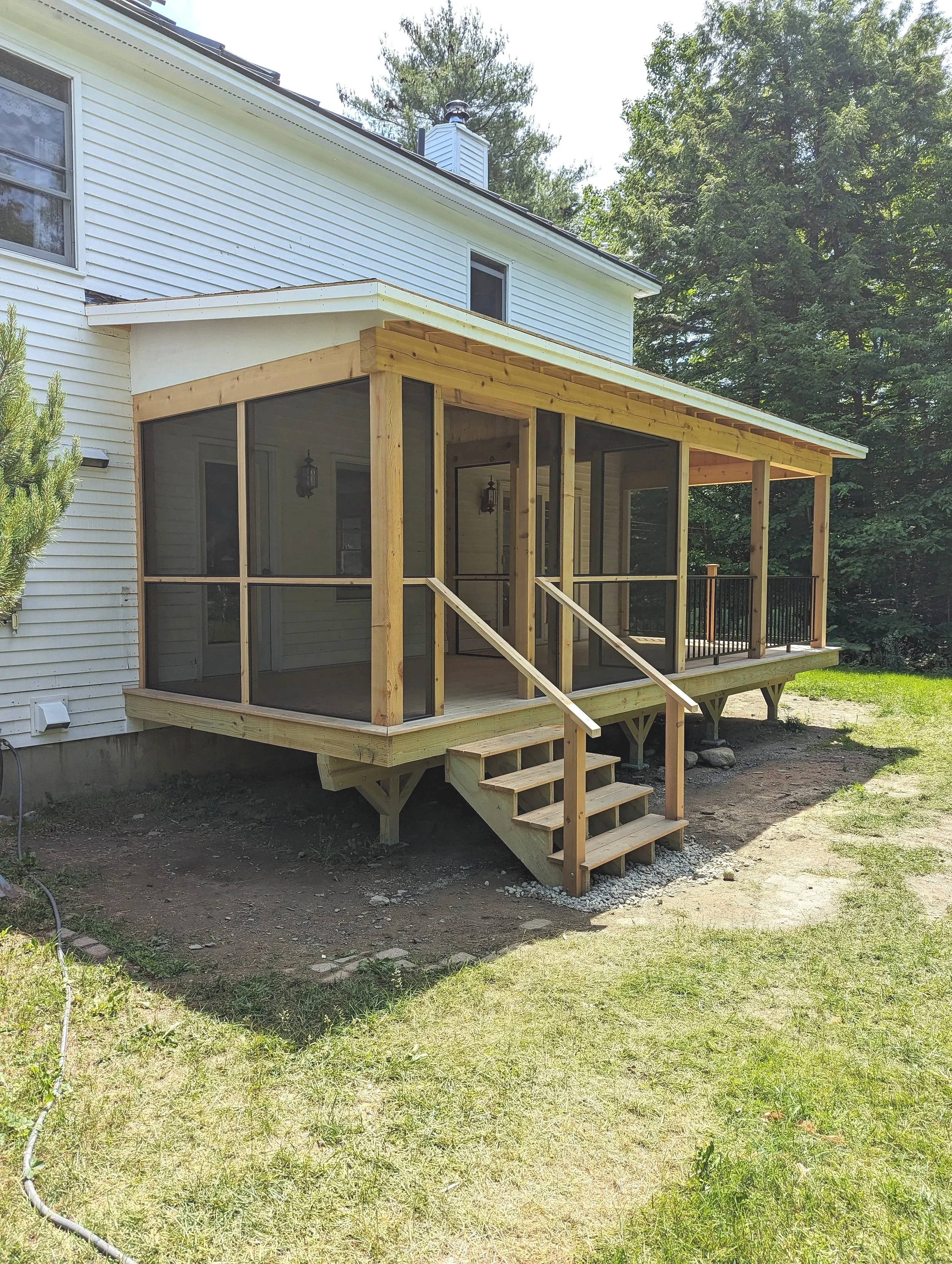 Newly built screened porch attached to a white house with a ramp and stairs, surrounded by trees and grass.
