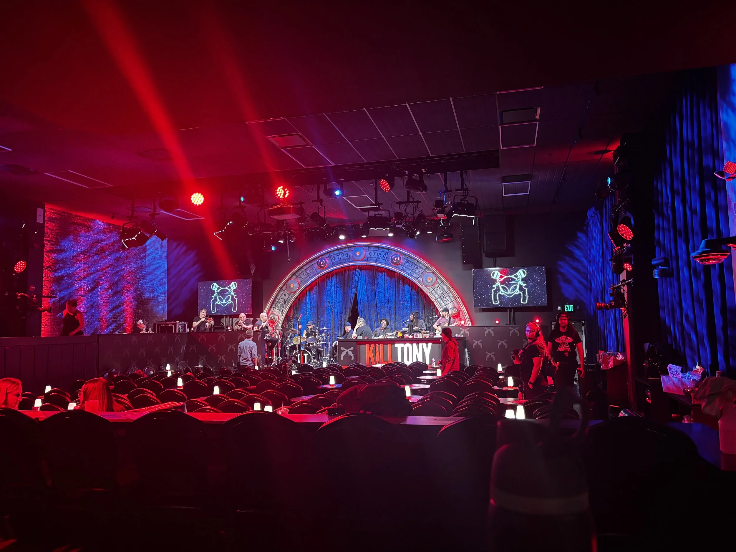 Concert stage with musicians performing and colorful lighting, audience seats in the foreground, large screens displaying graphics.