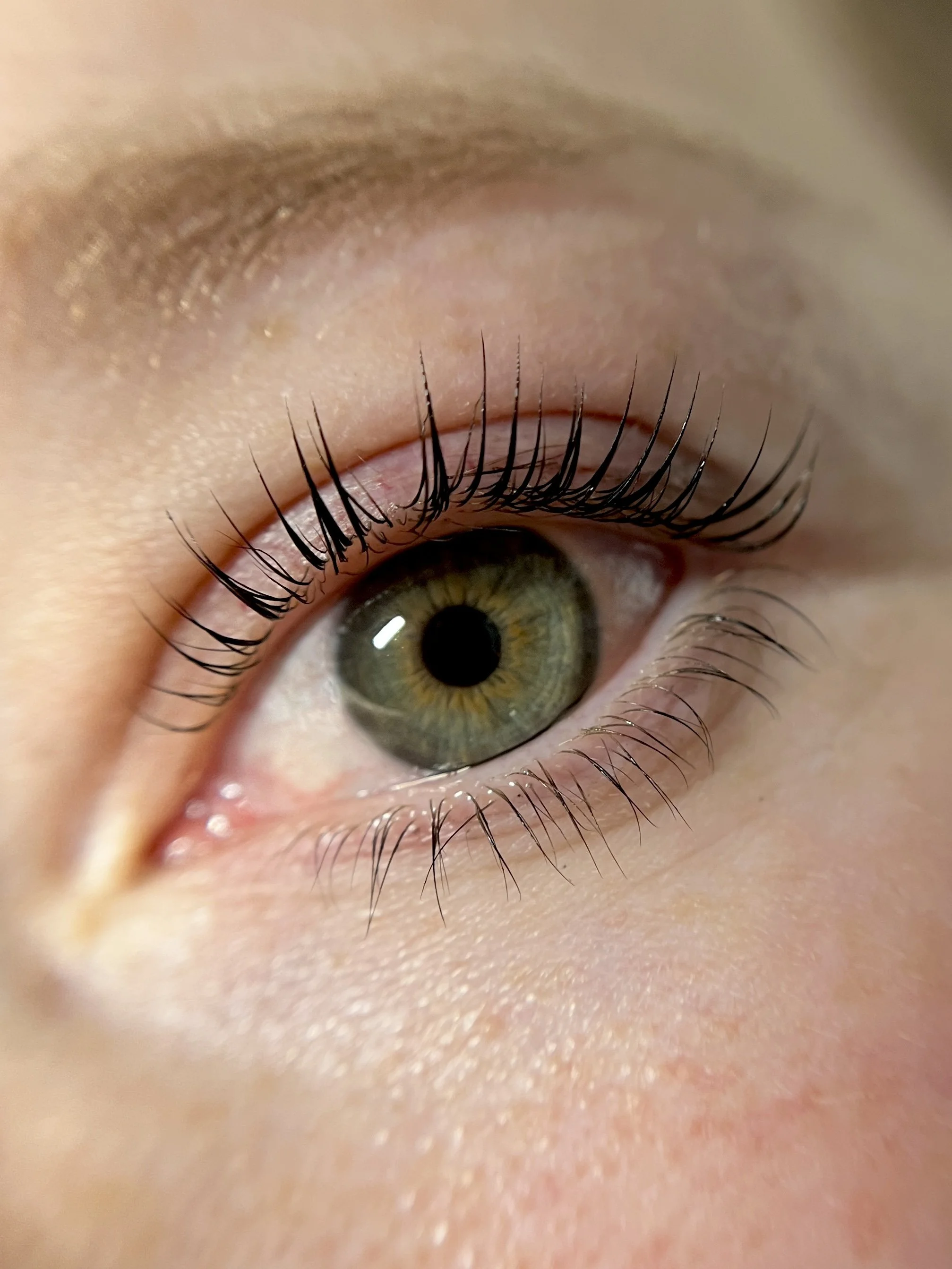 Close-up of a human eye with green iris and long lifted black tinted eyelashes.
