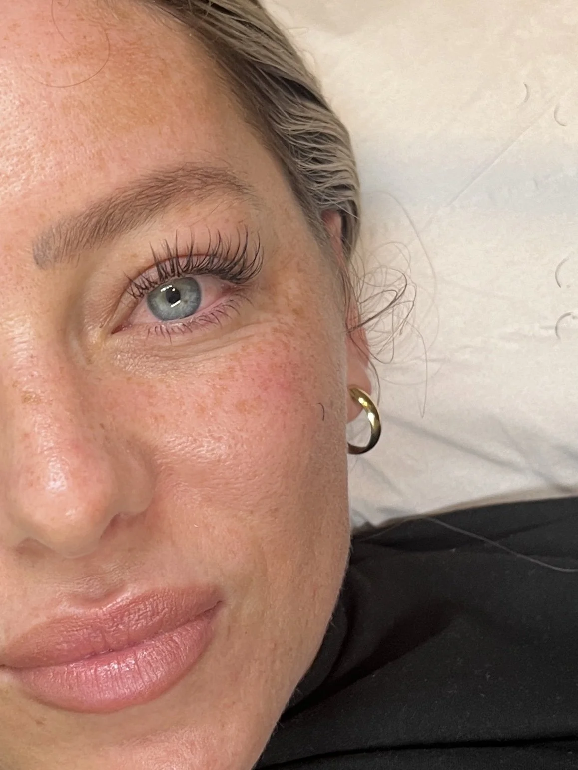 Close-up of a woman's face showing her eye, eyebrow, part of her nose, lips, and a gold hoop earring.
