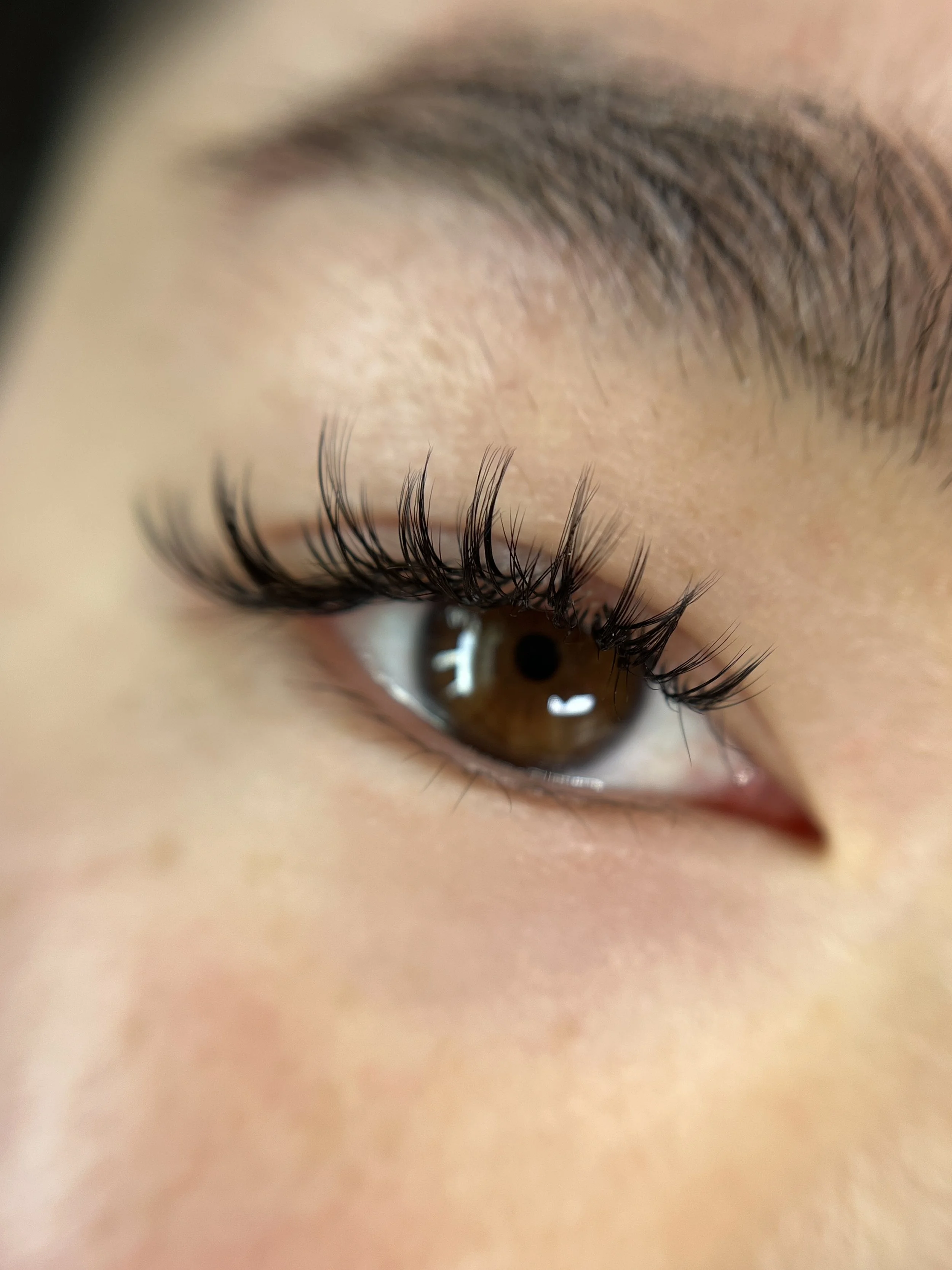 Close-up of a person's eye with brown iris, long curled eyelashes, and light skin.
