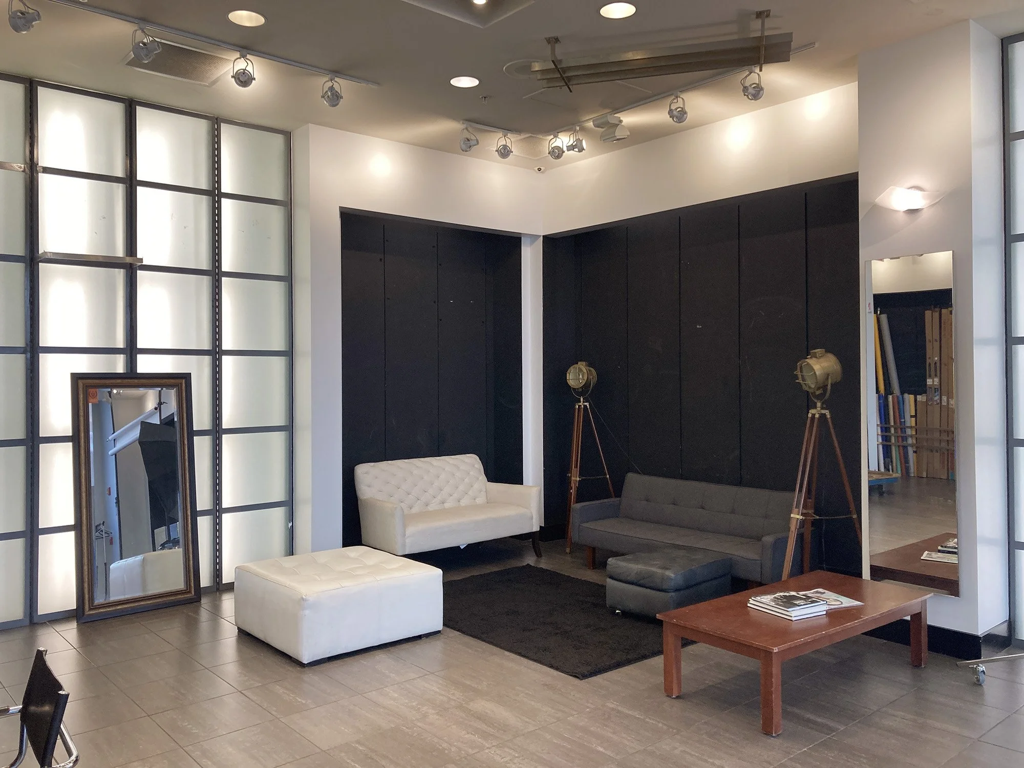 Modern interior lounge area with two sofas, minimalistic coffee table, large mirror, filming lights, and a black accent wall.