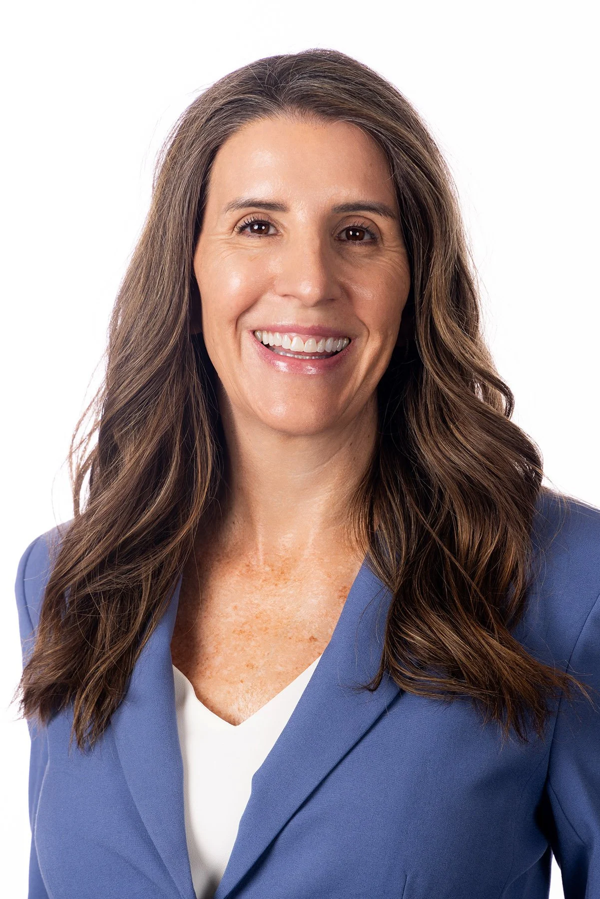 Headshot of a woman with long brown hair, wearing a blue blazer and smiling, against a plain white background. Salt Lake City Portrait & Headshot Photographer - Nick Sokoloff - Utah