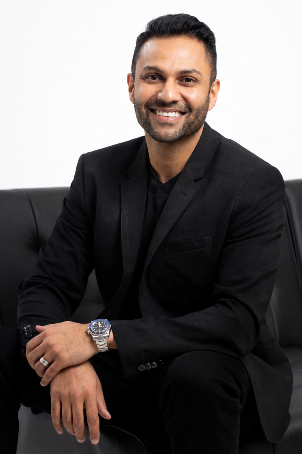 Contemporary environmental headshot of a smiling man wearing a black shirt and jacket. The relaxed pose and darker wardrobe create a modern personal branding portrait.
