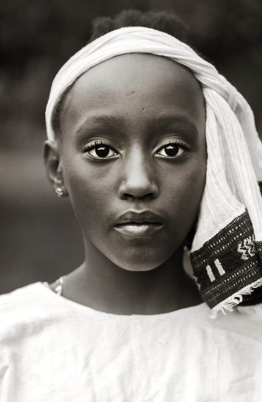 Close-up black and white portrait of a young woman with a head wrap, looking directly at the camera.