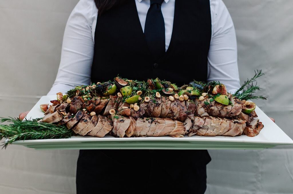  A server holding a large platter for grilled pork tenderloin with black and green figs 