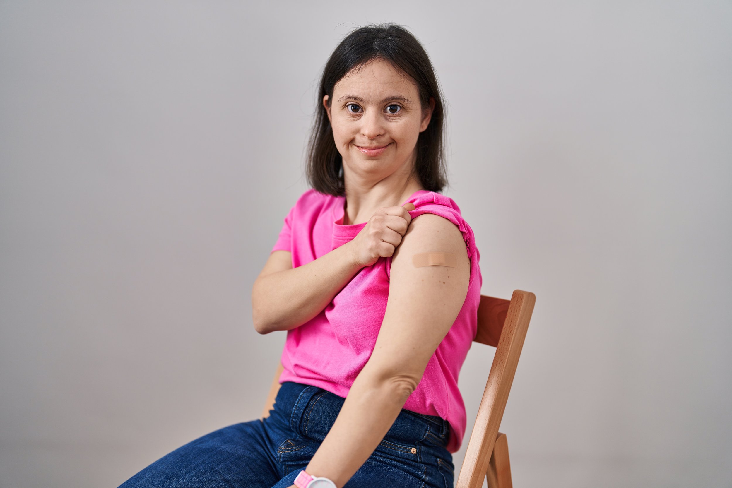 A neurodiverse person in a pink shirt showing off their vaccinated arm.