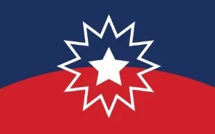 Juneteenth flag with a navy blue top half and red bottom half. In the center is a white star surrounded by a white starburst design where the two colors meet