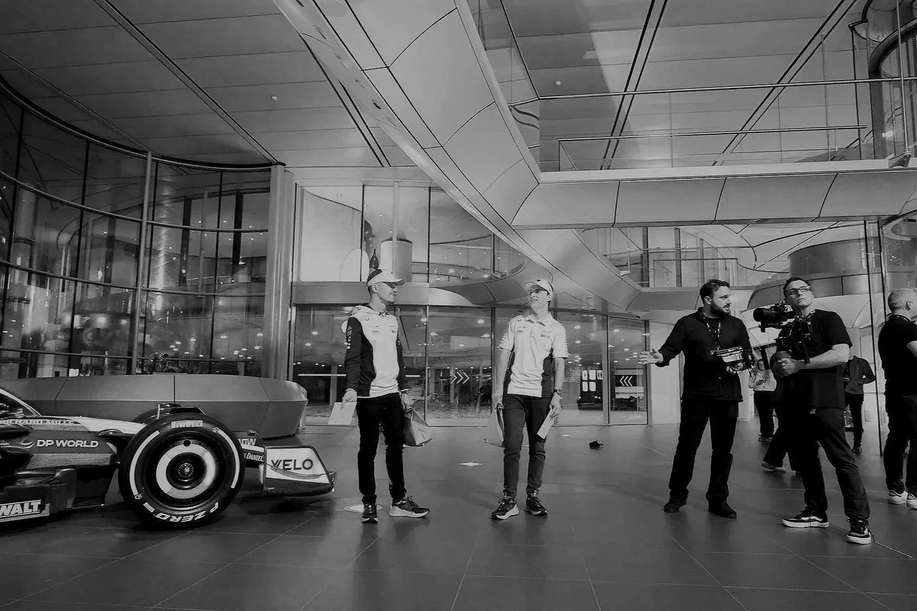 A black and white photo of a car and crew members in the McLaren HQ lobby with modern architectural design and large glass windows.