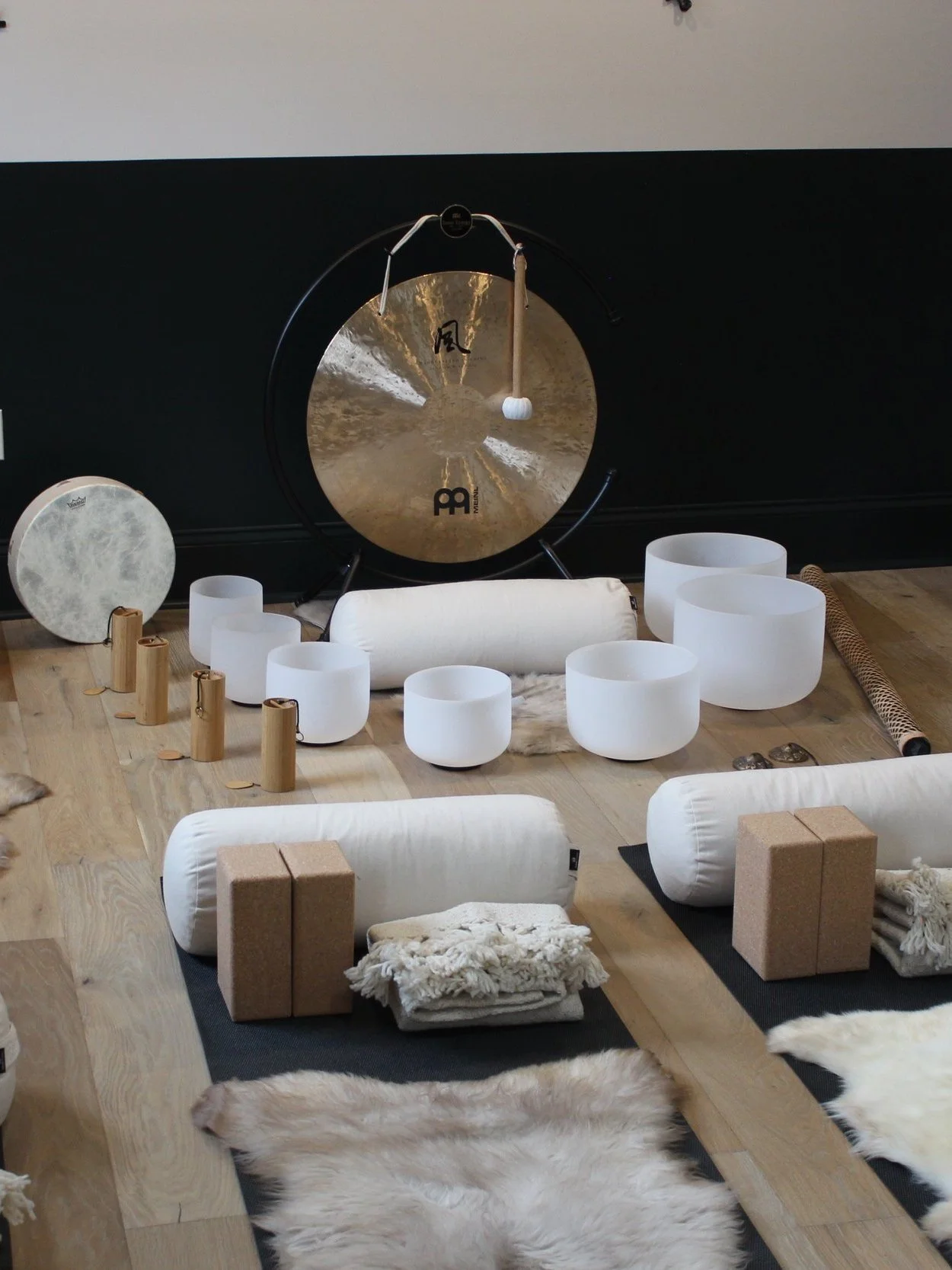 Meditation or yoga space with a large gong, white meditation cushions, fur rugs, and other sound therapy instruments in a calm, minimalist setting.