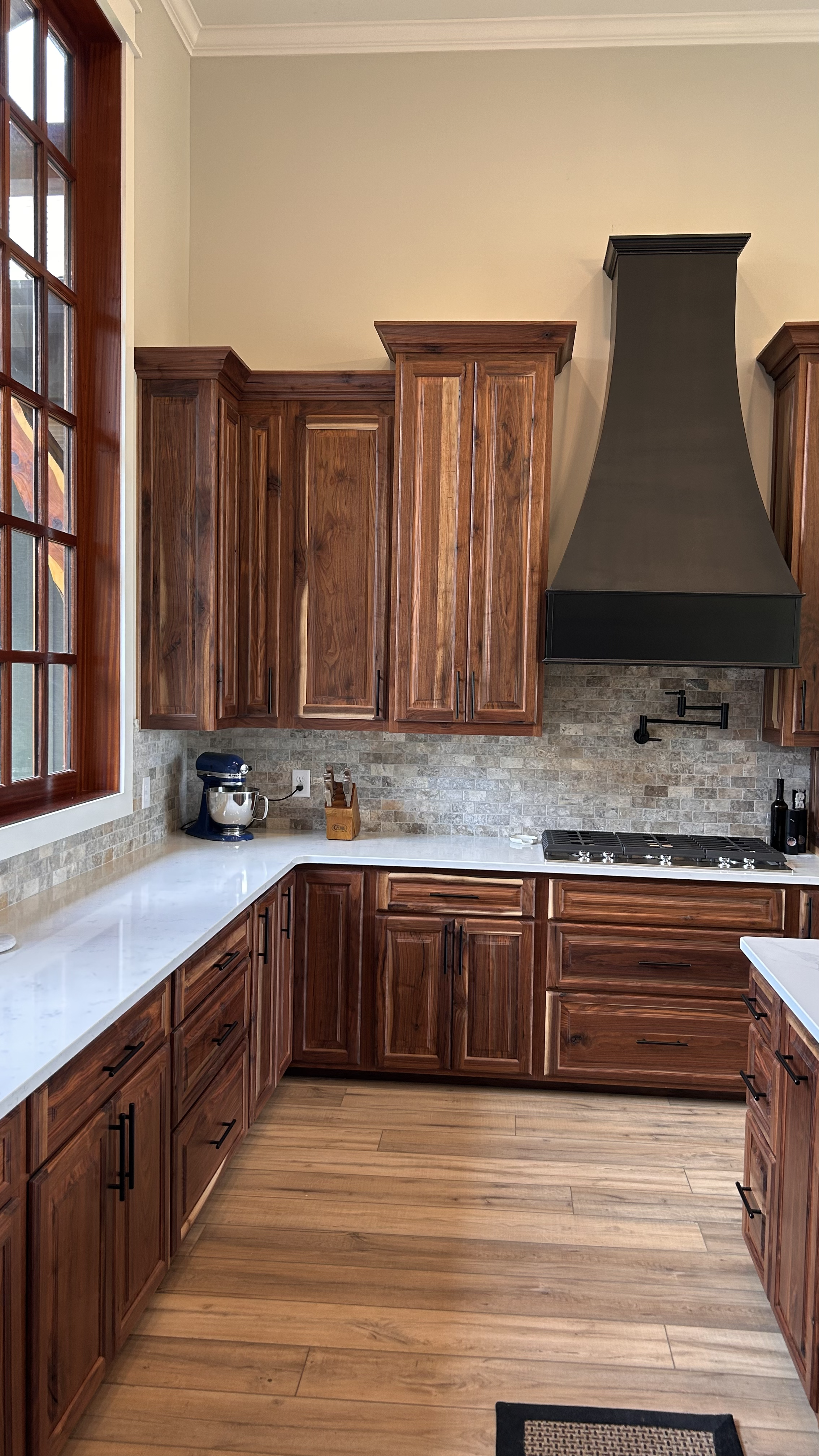 A kitchen with black walnut raised panel doors and custom curved black range hood.