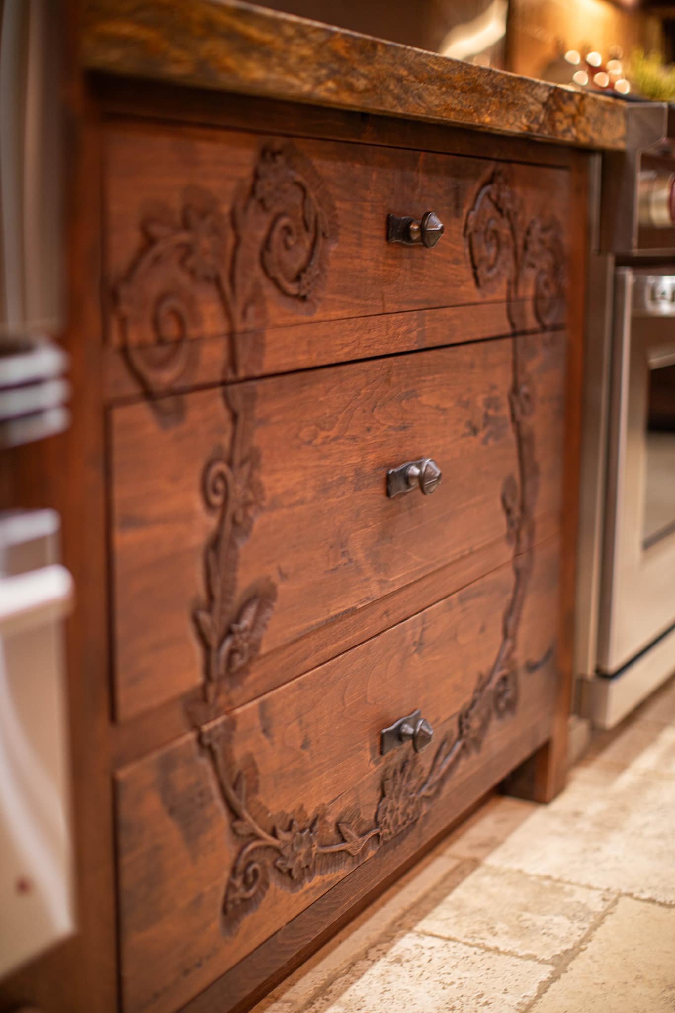 Close-up of a wooden dresser with ornate carvings and decorative metal handles, placed on a tiled floor.