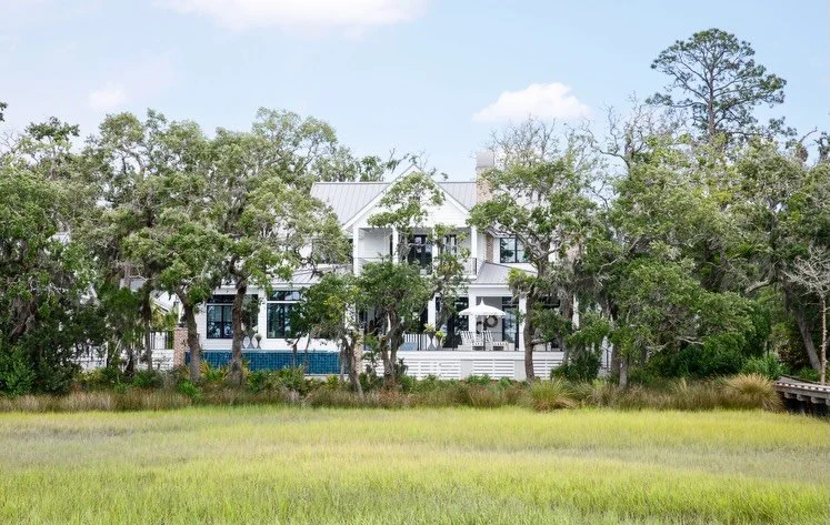 From a distance, the house steals the show&mdash;timeless, confident, impossible to miss. But step a little closer and the real magic reveals itself: an upstairs porch made for lingering. Swing beds, soft color, marsh views, and the kind of calm you 